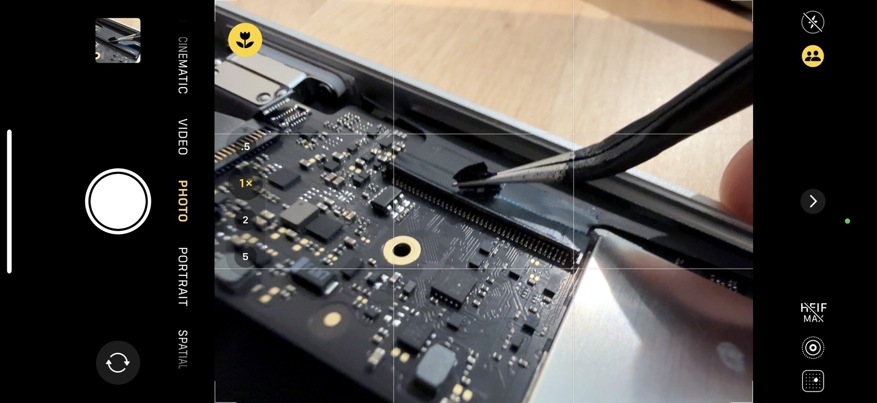 Screenshot of camera app on iPhone in macro mode, framing a pair of tweezers pulling tape from a connector on a black PCB